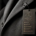 New York Fashion Act: a tailored wool coat's hangtag printed with a New York State outline and compliance checkmarks, macro product shot